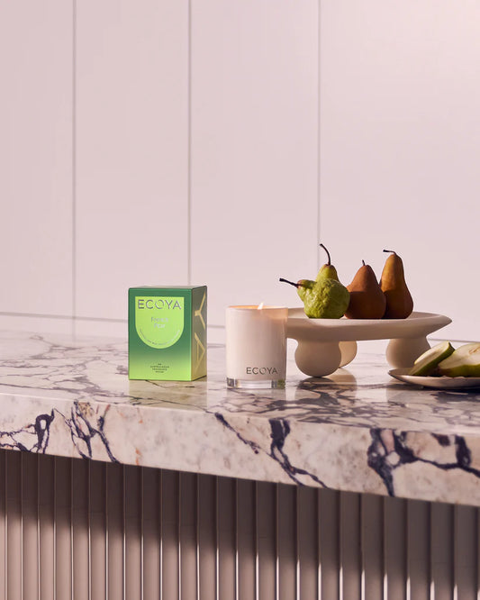 A candle accompanied by a bowl of ripe pears and a bowl of colorful fruit, evoking a sense of comfort and elegance.