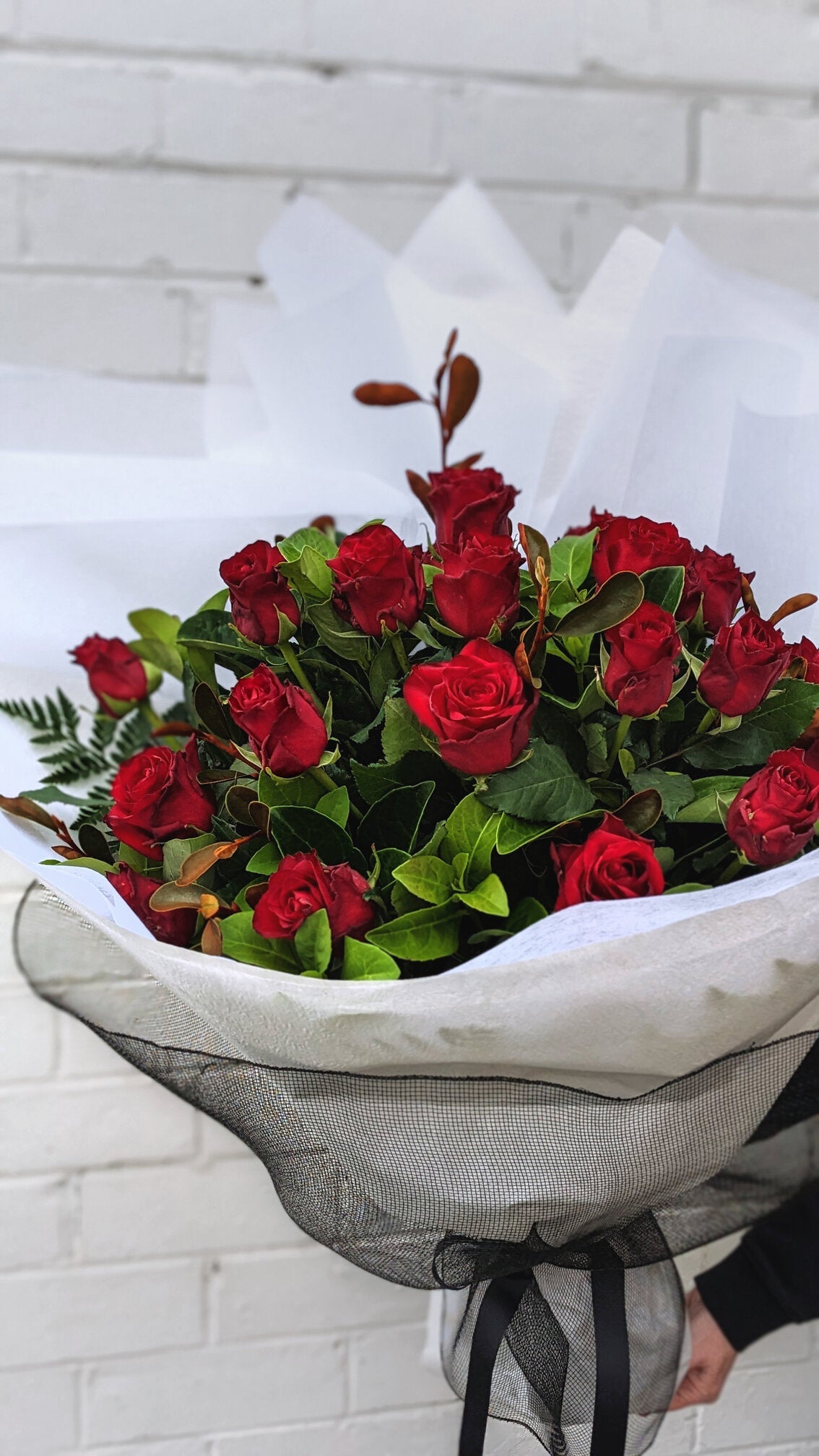 A bouquet of red roses wrapped in a gray cloth with a black ribbon, held by a person.