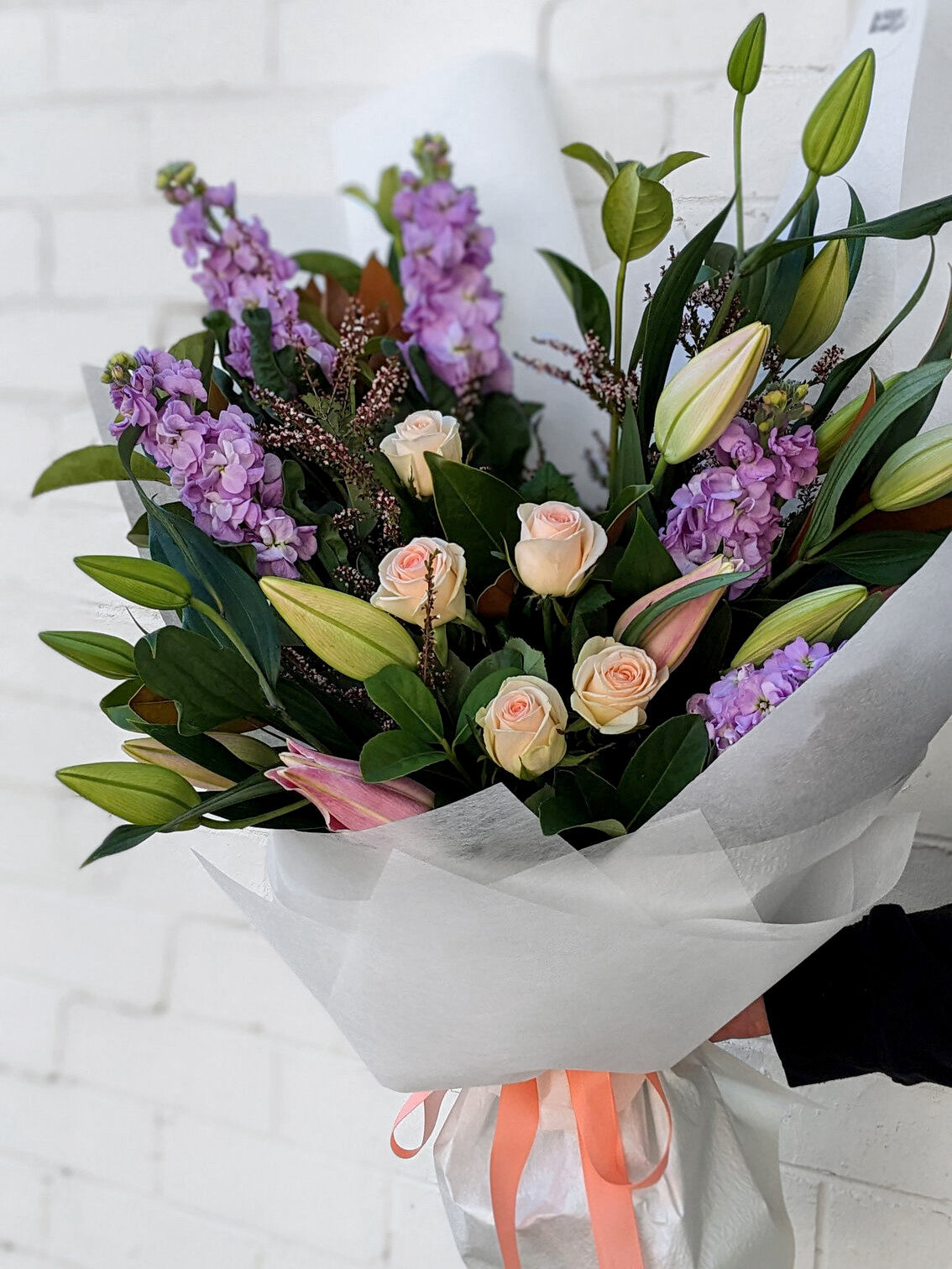 Charming arrangement of purple and pink flowers displayed in a simple white paper bag.
