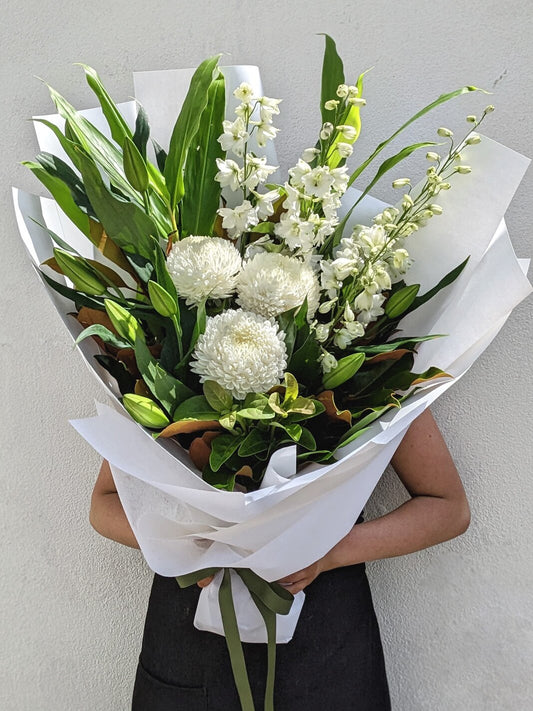 A person holding a large bouquet of white flowers wrapped in paper.