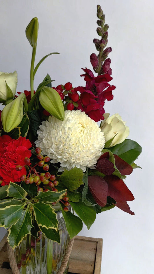 A vibrant floral arrangement with red blooms, a large white chrysanthemum, and green leaves in a vase.