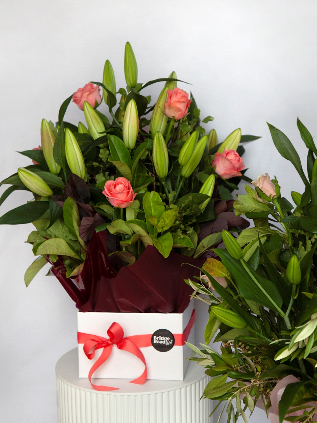 A pristine white vase showcasing red roses complemented by green leaves, creating a striking and elegant floral arrangement.