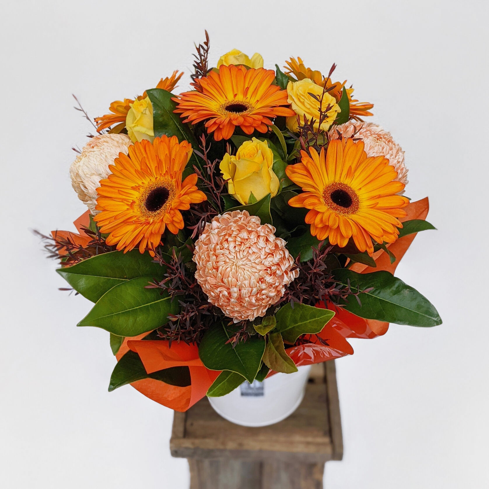 A vibrant bouquet of orange gerberas, yellow roses, and assorted blooms in a vase.