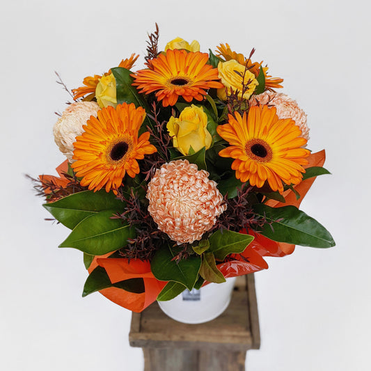 A vibrant bouquet of orange gerberas, yellow roses, and assorted blooms in a vase.