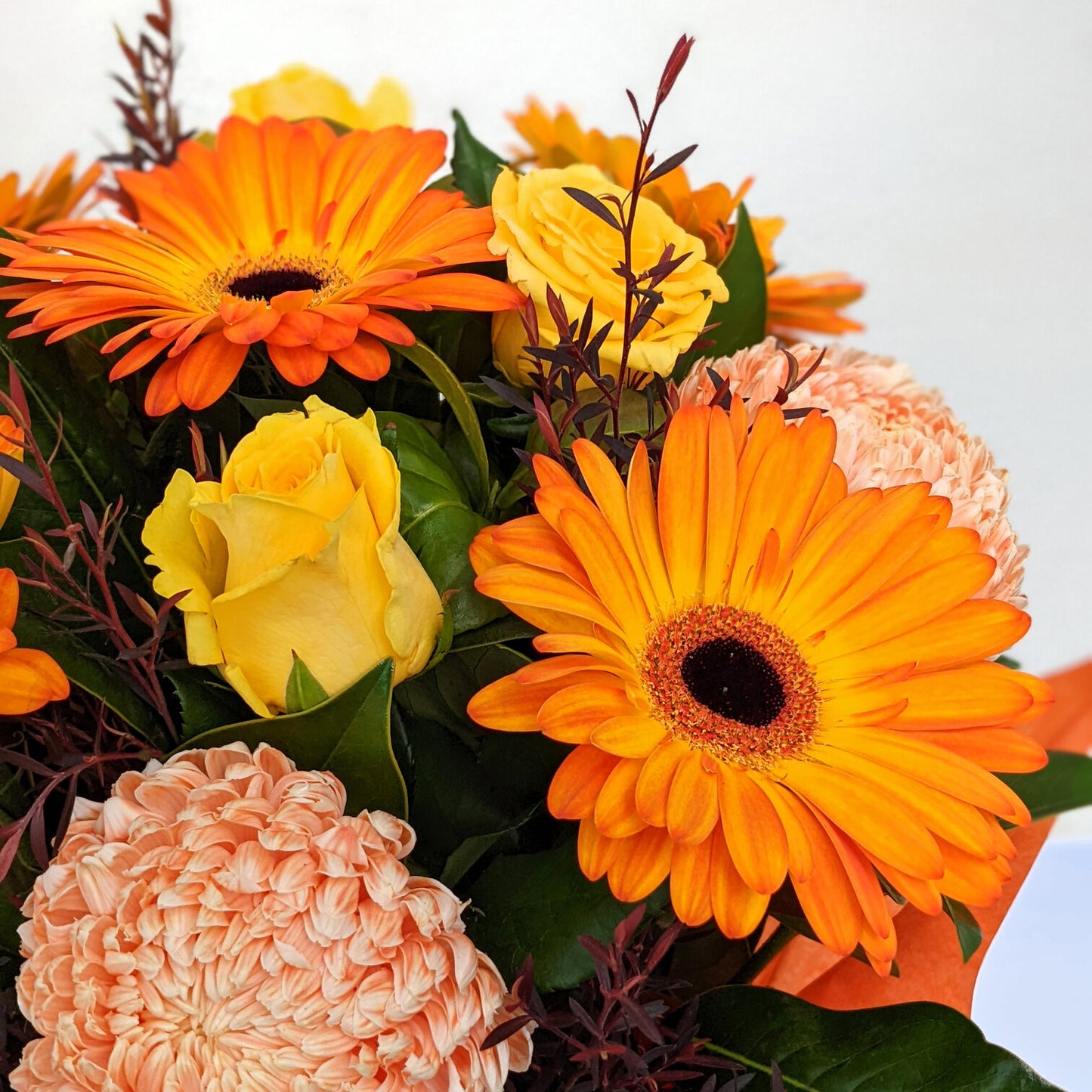 Bright bouquet with orange gerberas, yellow roses, and pink flowers.