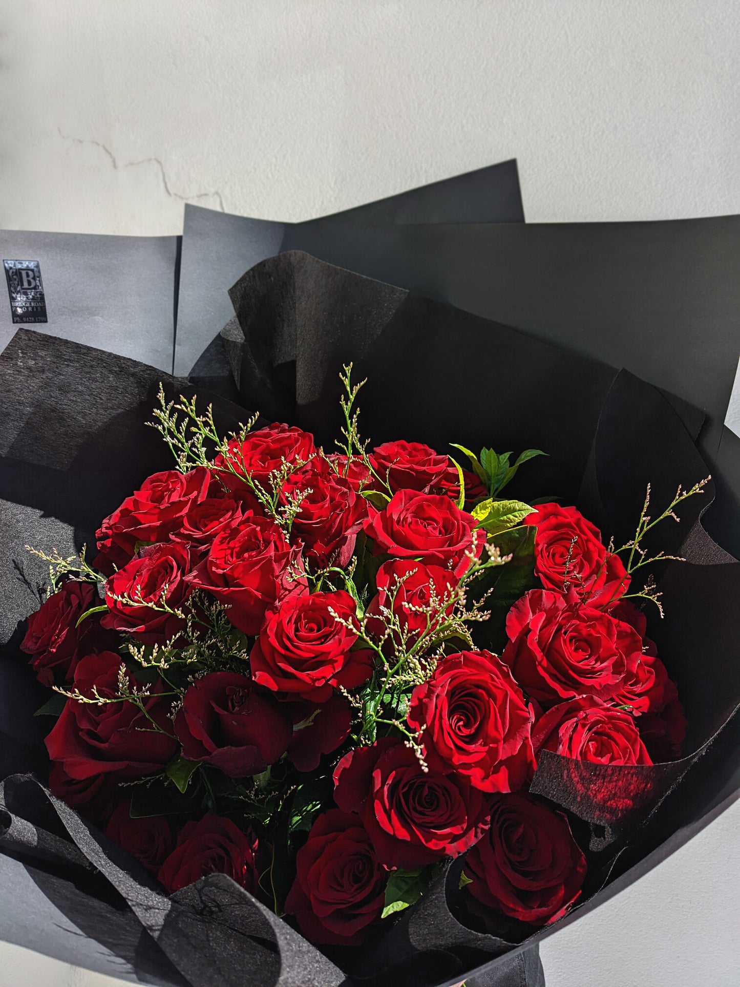 A bouquet of red roses wrapped in black paper, bathed in natural light.