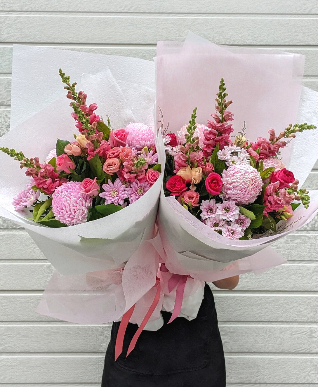 Two large pink floral bouquets with ribbons held by a person against a white background.