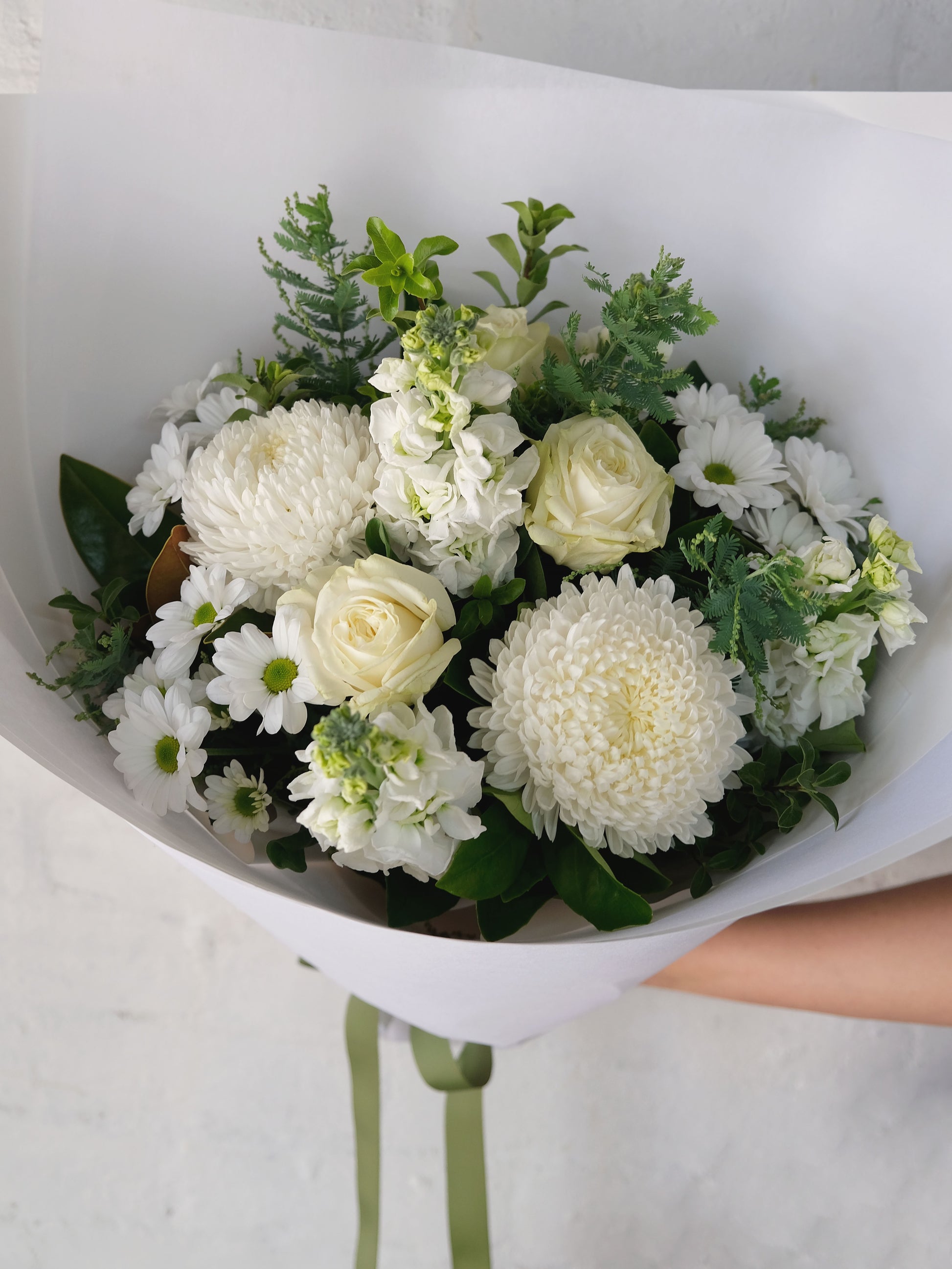 A bouquet of white flowers including roses and chrysanthemums wrapped in white paper.