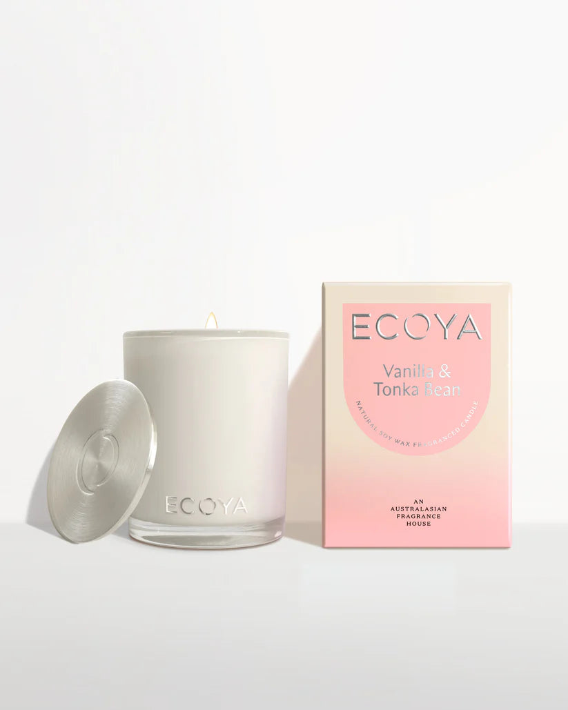 A reed diffuser on a wooden tray, a lit candle, and a box labeled "ECOYA" by a sunlit window.