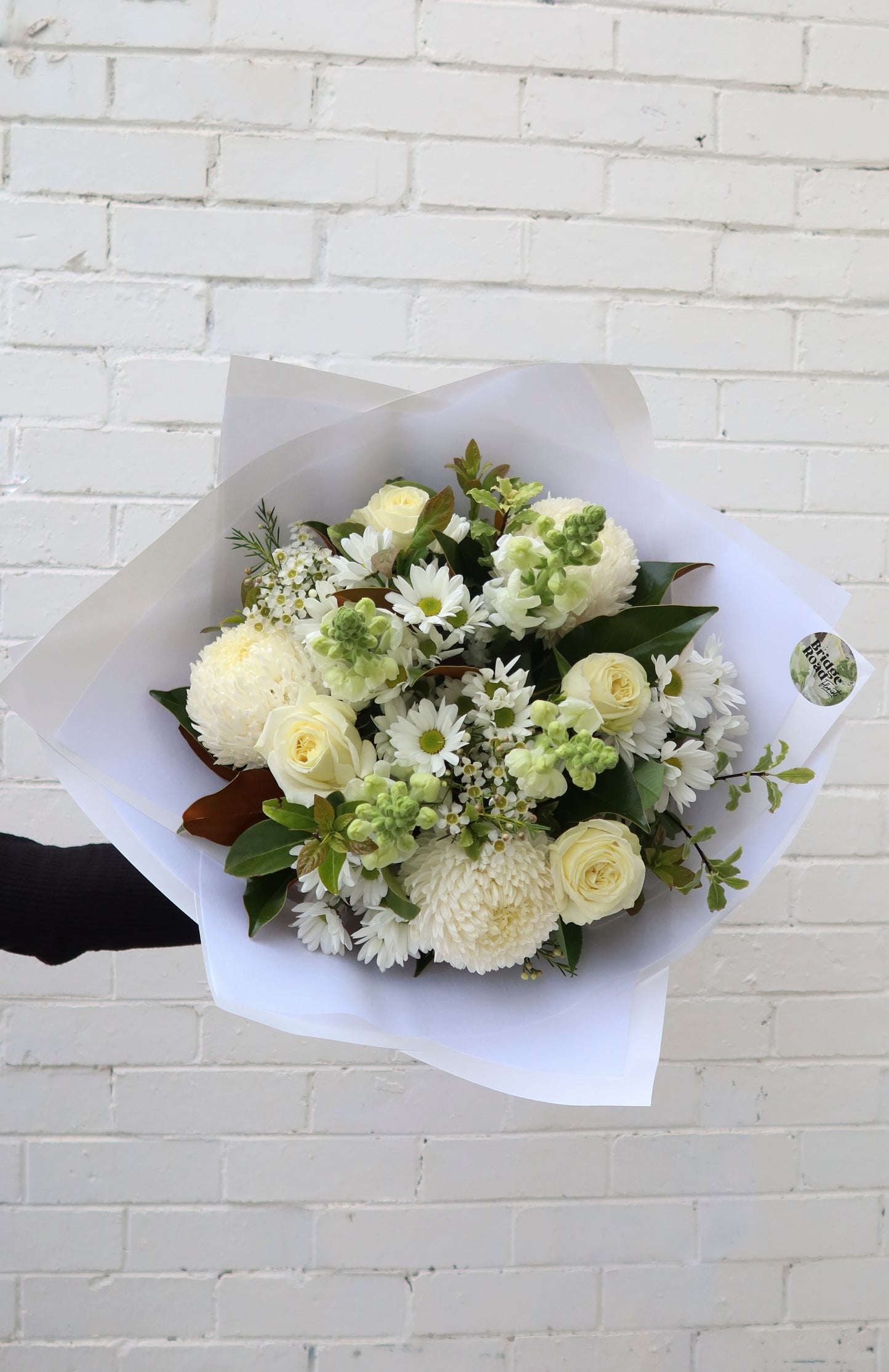 Person holding a bouquet of white flowers against a brick wall.