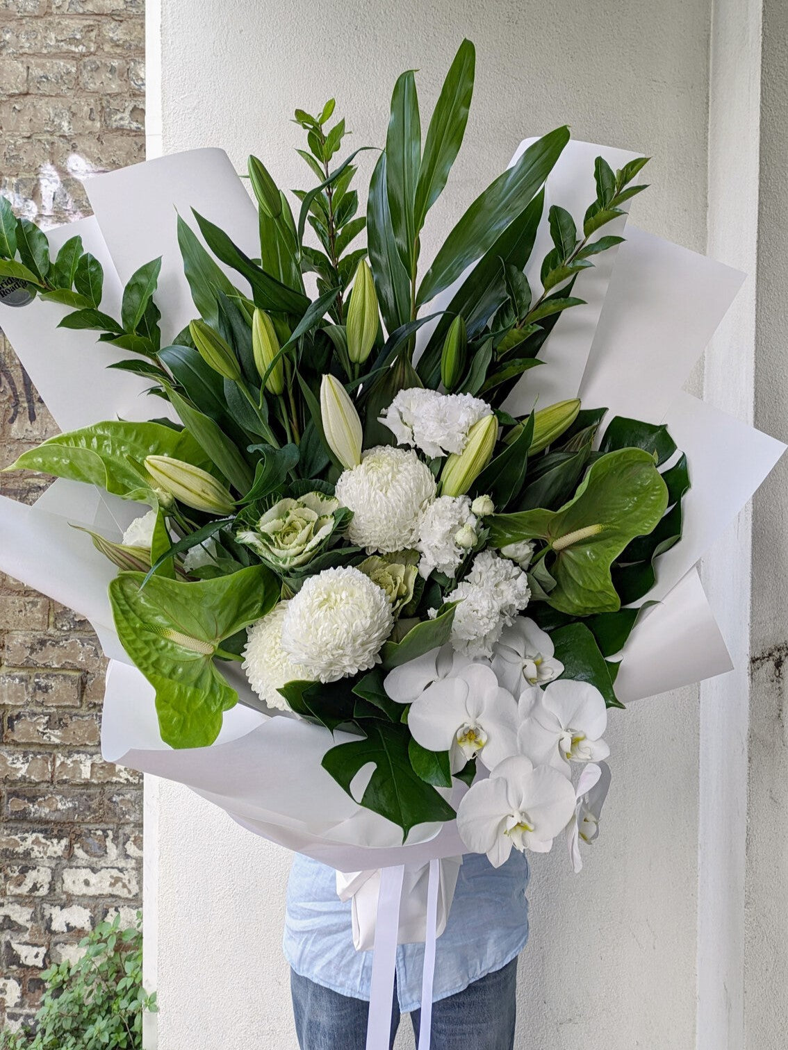 Person holding a large bouquet of white flowers wrapped in white paper.
