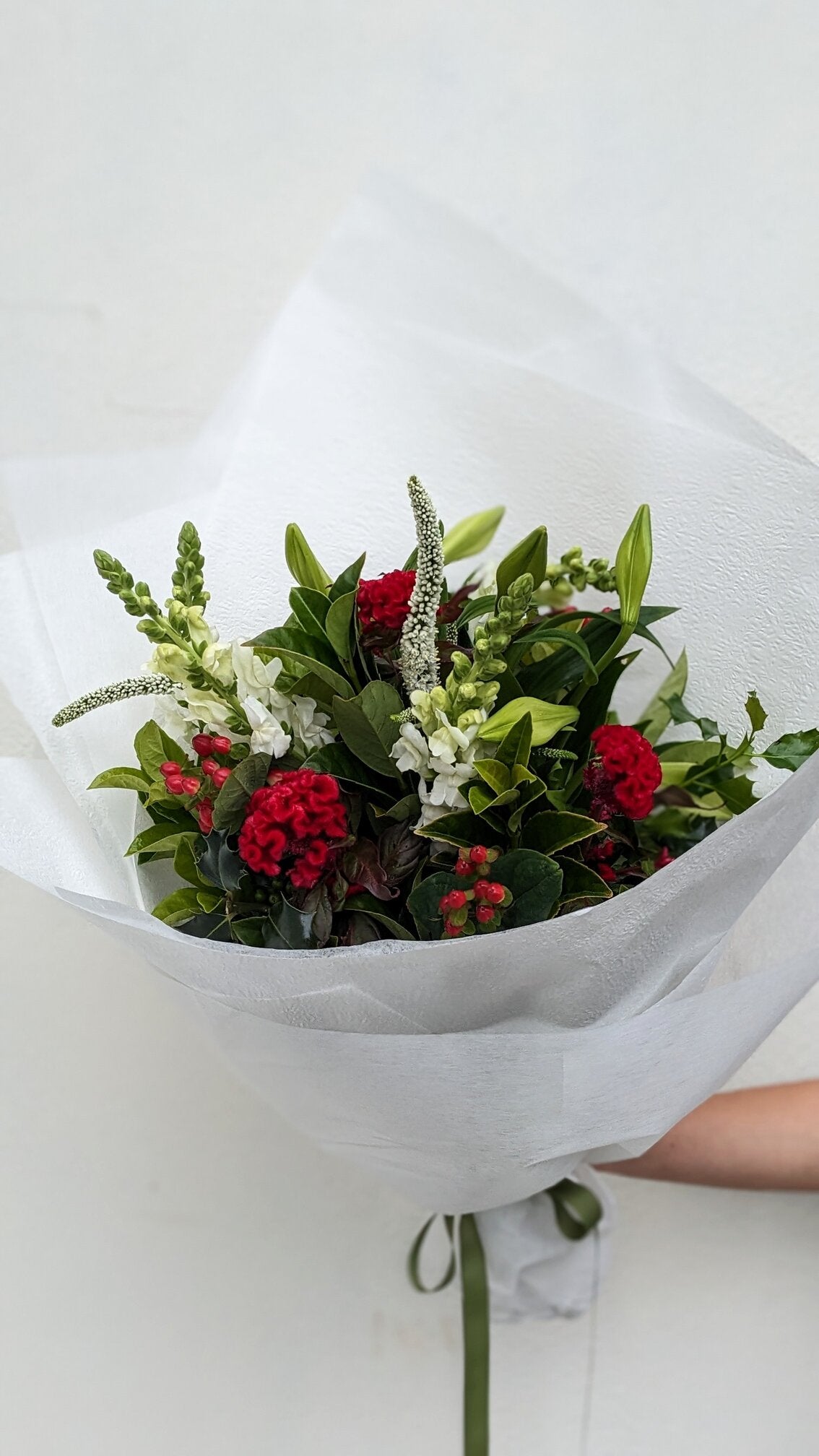 Bouquet of red and white flowers wrapped in white paper held by a person.