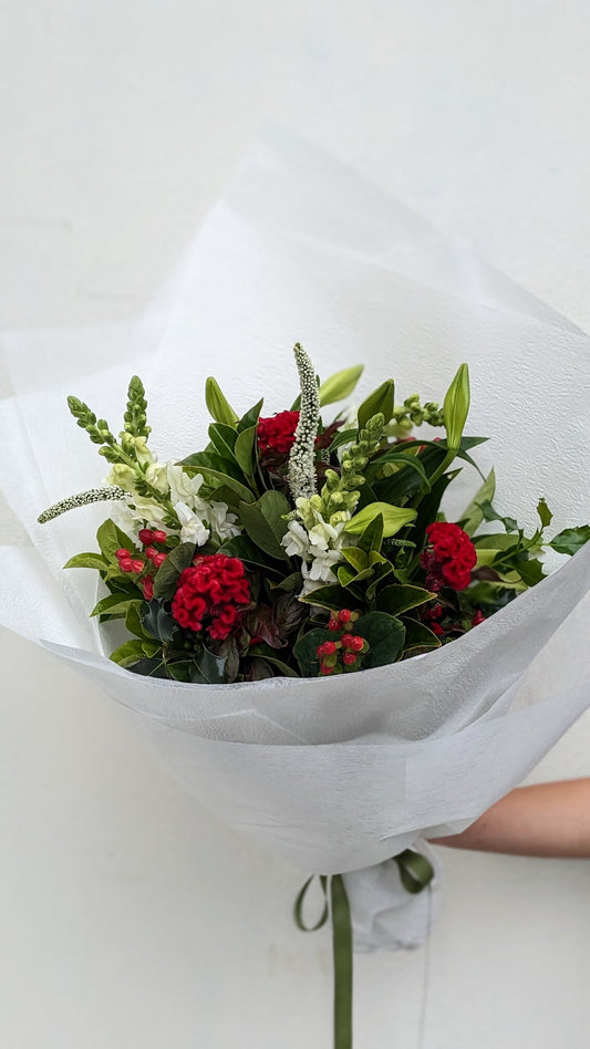 Bouquet of red and white flowers wrapped in white paper held by a person.